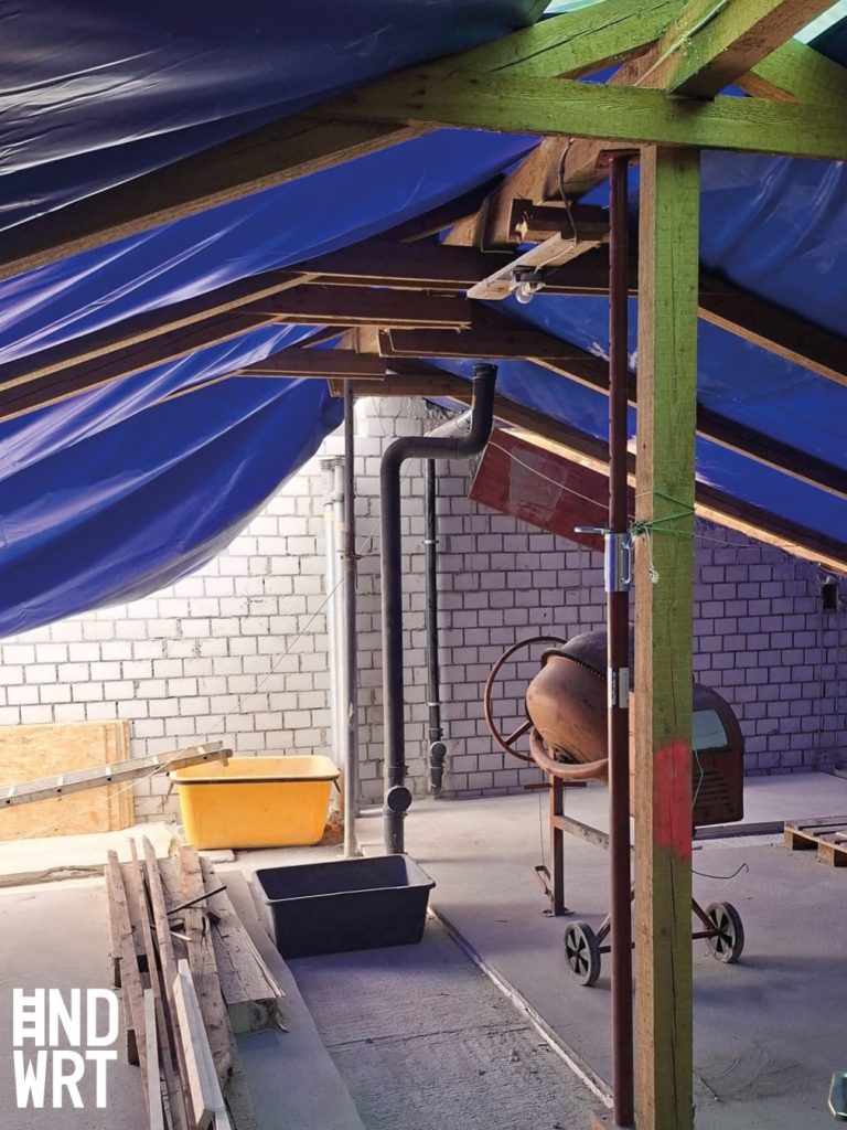 Dachgeschoss im Rohbau mit sichtbarem Holzsparren, blauer Dampfbremsfolie, weißem Mauerwerk und provisorischer Plane