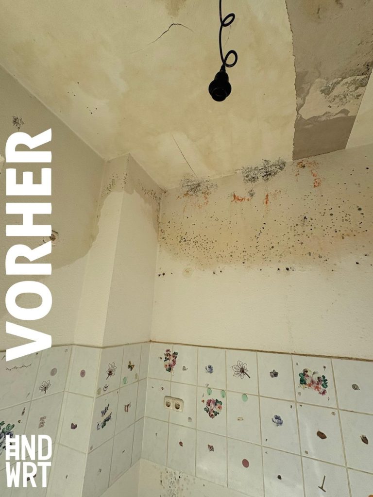 Raumecke mit Wasserschaden, Decke und Wände mit Feuchteflecken und Schimmelbefall, unten Wandfliesen mit Blumenmuster