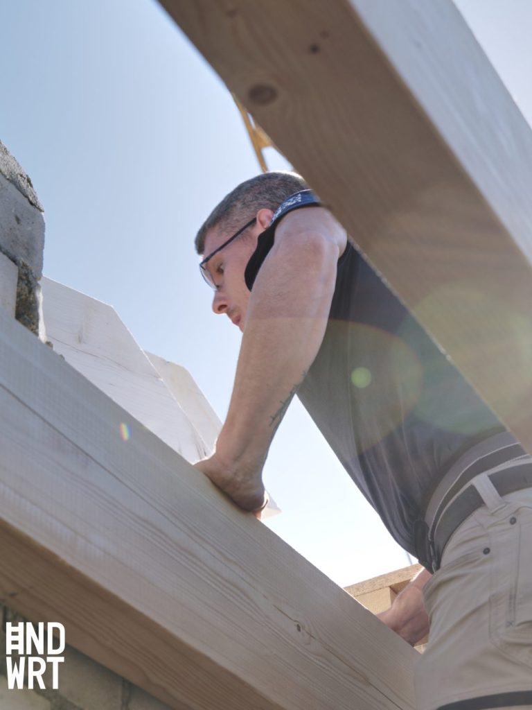 Ein Mann in Arbeitskleidung befestigt etwas auf der Holzkonstruktion.