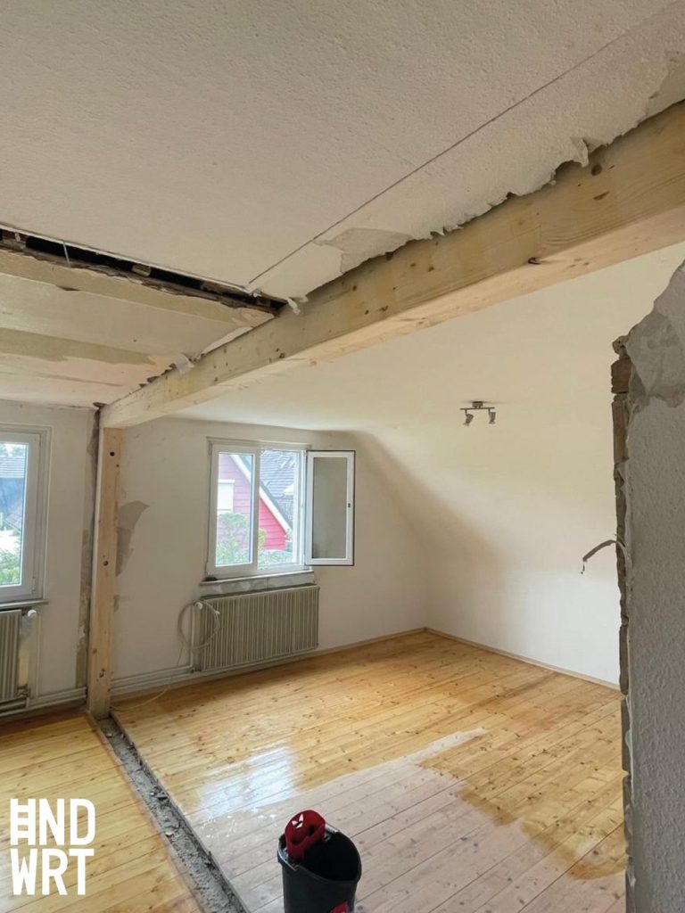Raum mit Holzdielenboden während Abbrucharbeiten, teilweise entfernte Deckenverkleidung und freiliegende Holzbalken