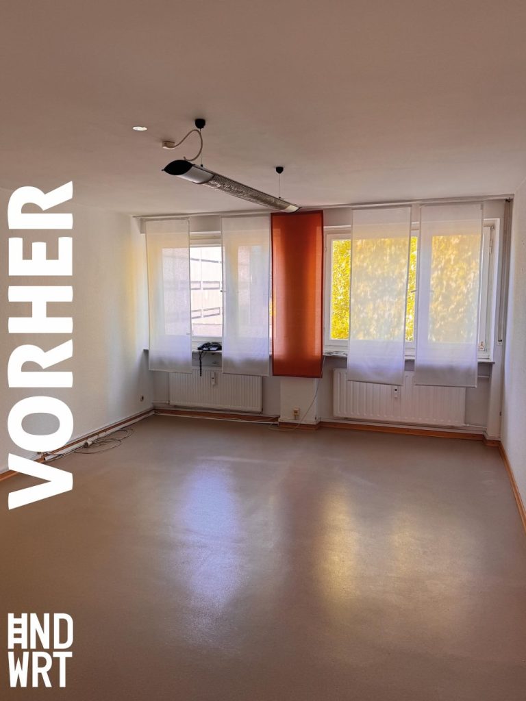 Leerer Raum mit grauem Bodenbelag, weißen Wänden, Heizkörpern unter Fenstern und orangefarbenem Deckenelement