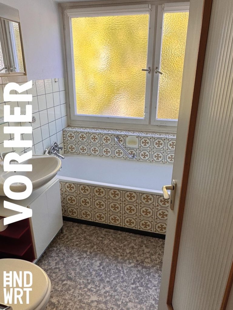 Badezimmer vor Sanierung mit gemustertem Fliesenboden, gefliester Badewanne, Waschbecken und Fenster mit gelbem Ornamentglas