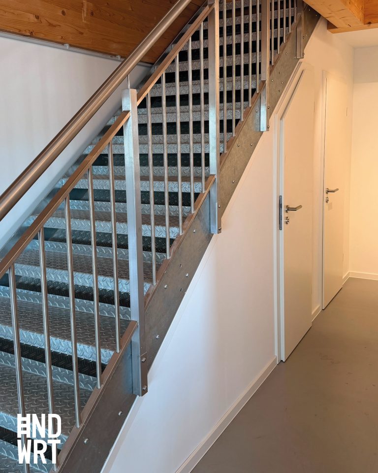 Treppenhaus mit Metallstufen und Edelstahlgeländer, weiße Innentüren mit Edelstahl-Drückergarnitur, Holzdecke
