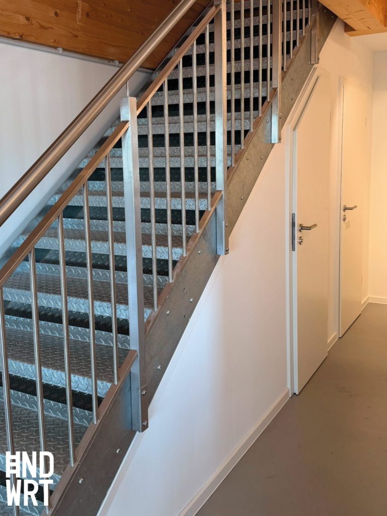 Treppenhaus mit Metallstufen und Edelstahlgeländer, weiße Innentüren mit Edelstahl-Drückergarnitur, Holzdecke