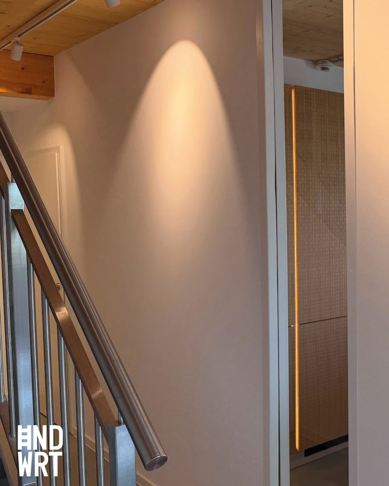 Treppenhaus mit Holzdecke, weißer Wand, Edelstahlhandlauf und moderner Glastür mit LED-Beleuchtung