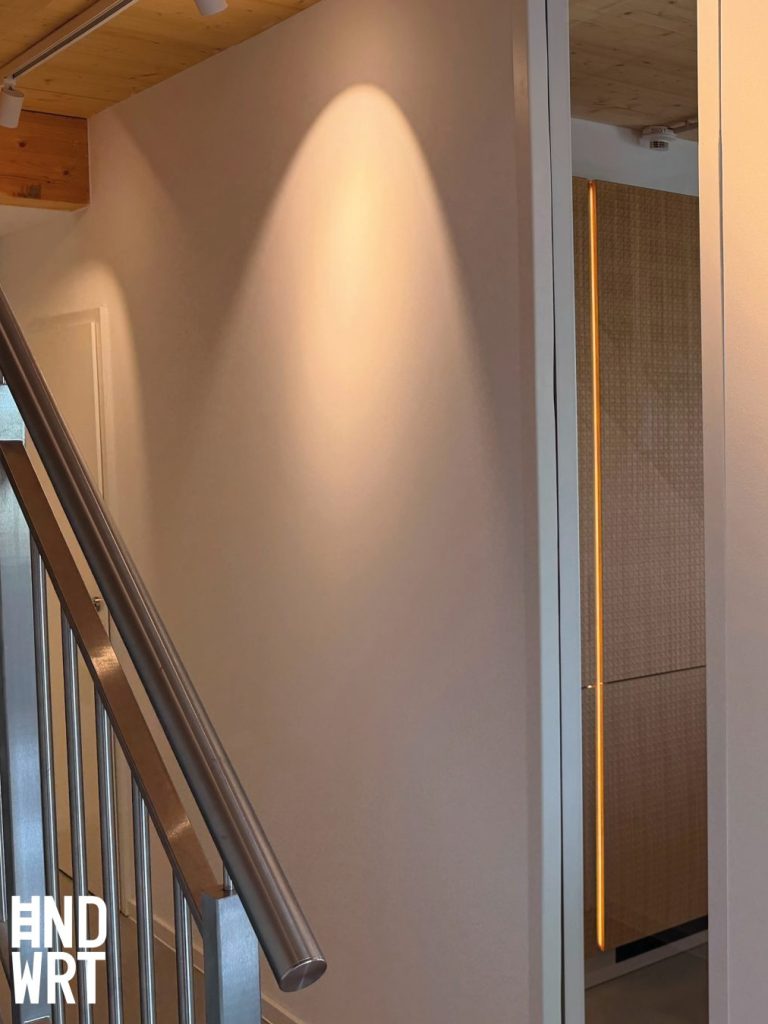 Treppenhaus mit Holzdecke, weißer Wand, Edelstahlhandlauf und moderner Glastür mit LED-Beleuchtung