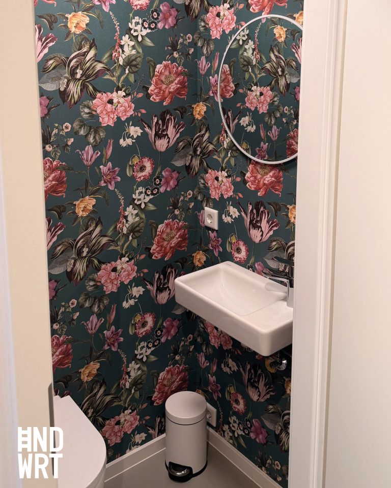 Gäste-WC mit dunkelgrüner Blumentapete, weißem Handwaschbecken, rundem Wandspiegel und Tretmülleimer