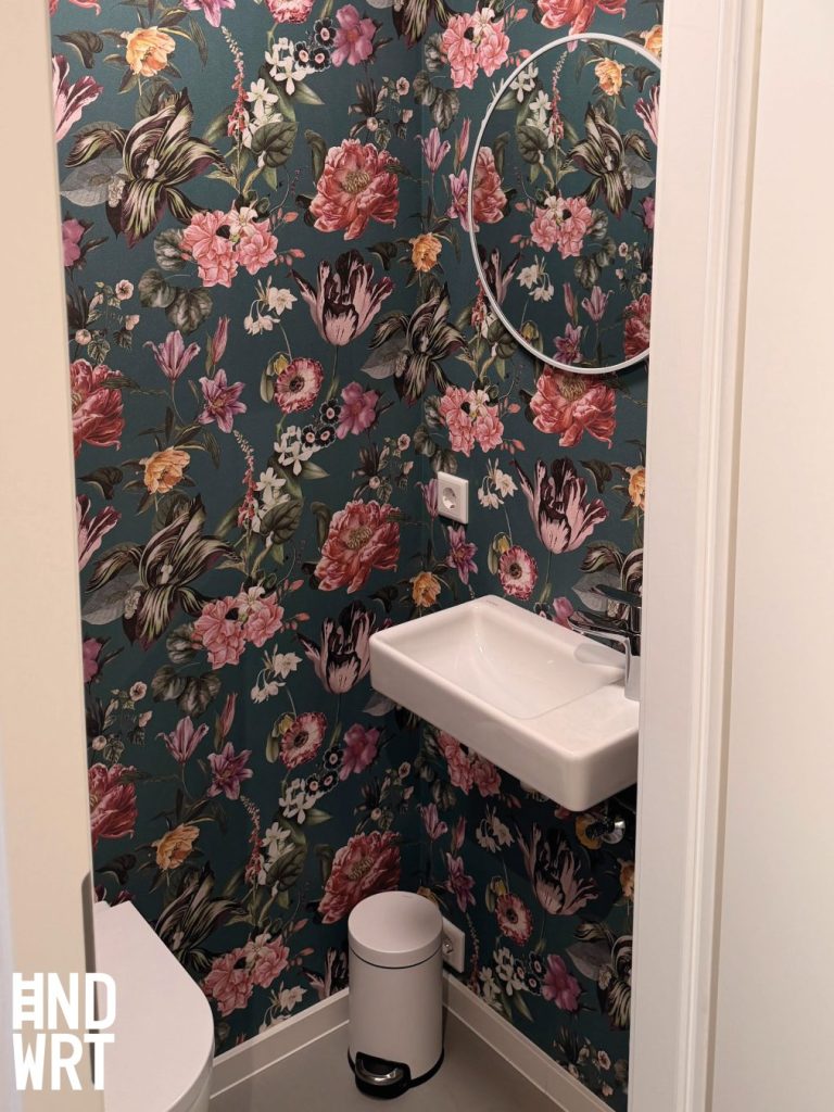 Gäste-WC mit dunkelgrüner Blumentapete, weißem Handwaschbecken, rundem Wandspiegel und Tretmülleimer