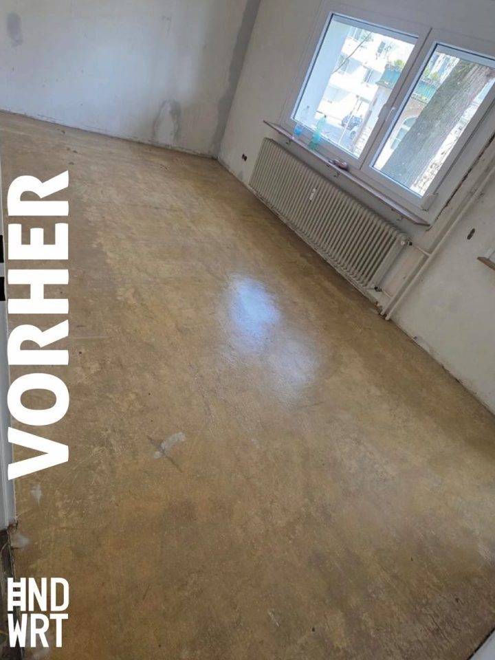 Leerer Raum mit altem Estrich, weißen Wänden, Rippenheizkörper unter zwei Fenstern, Vorher-Zustand einer Sanierung