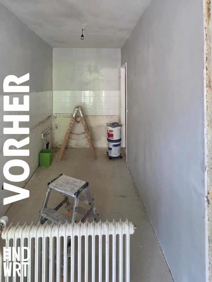 Raum während der Sanierung mit teils gefliesten Wänden, Leiter, Farbeimer und Estrichboden