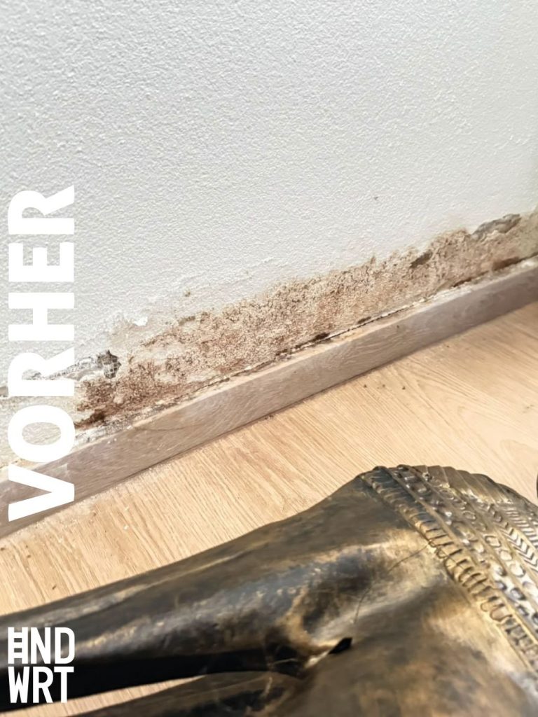 Feuchtigkeitsschaden an weißer Wand mit abgeplatztem Putz und Salzausblühungen über Holzfußleiste auf Parkettboden