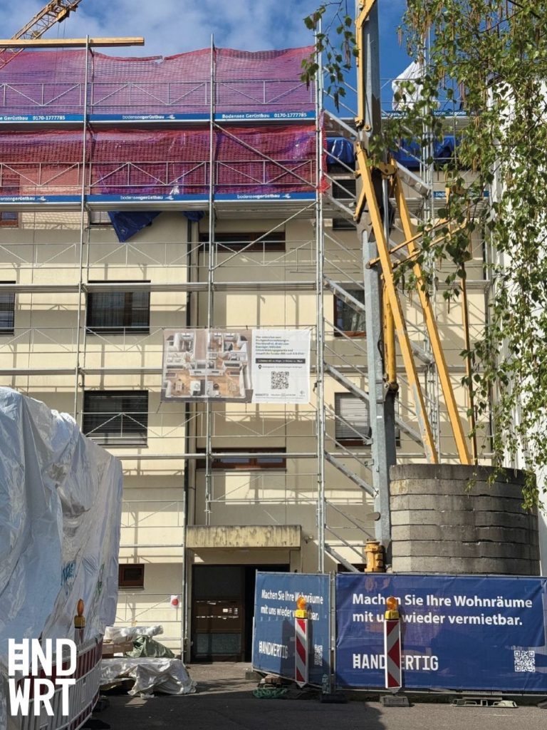 Mehrgeschossiges Wohngebäude mit Fassadengerüst, Schutznetz und Kran während laufender Sanierungsarbeiten