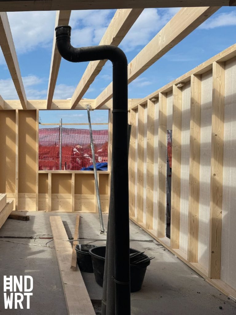 Schwarzes Ofenrohr mit Bogen in Holzrahmenbau, offene Dachkonstruktion mit Sparren, Betondecke, Rohbauphase