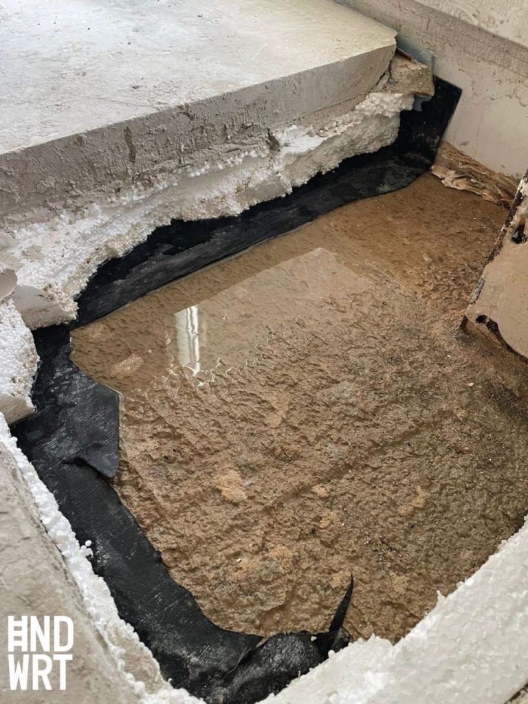 Teilweise entfernter Bodenbelag mit sichtbarer schwarzer Kleberschicht und beigem Estrich an Wand und Boden