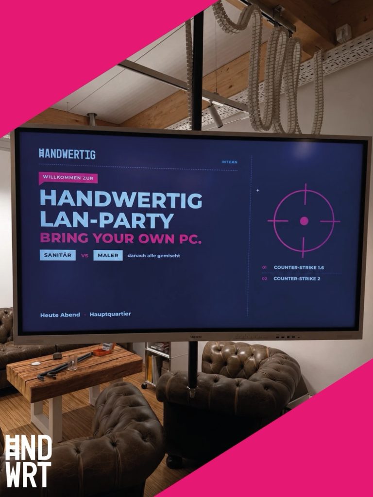 Großer Bildschirm zeigt Einladung zu einer LAN-Party in einem Raum mit Holzdecke und Polstermöbeln