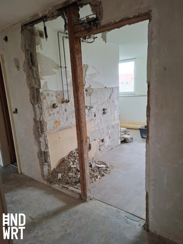 Durchbruch in Wand mit freiliegenden Holzbalken, Elektroleitungen und Schuttablagerungen während Sanierungsarbeiten